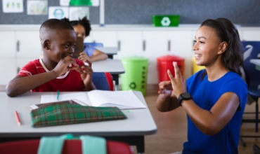 A young black boy and a teacher using sign language in a classroom setting.