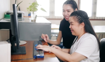 A person helping a child with a disability on a computer
